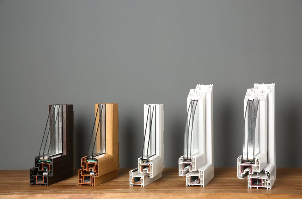 Profils de fenêtres en coupe, bois, PVC et aluminium alignés sur un établi
