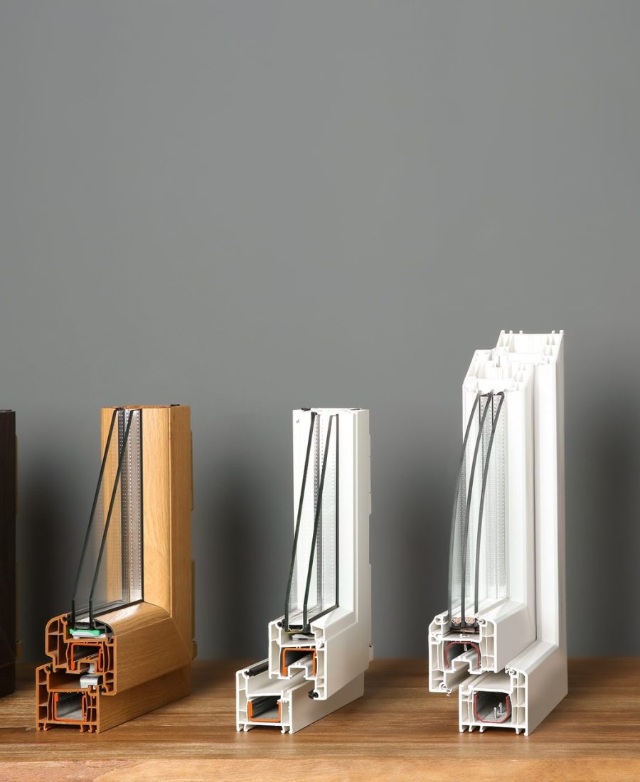 Profils de fenêtres en coupe, bois, PVC et aluminium alignés sur un établi